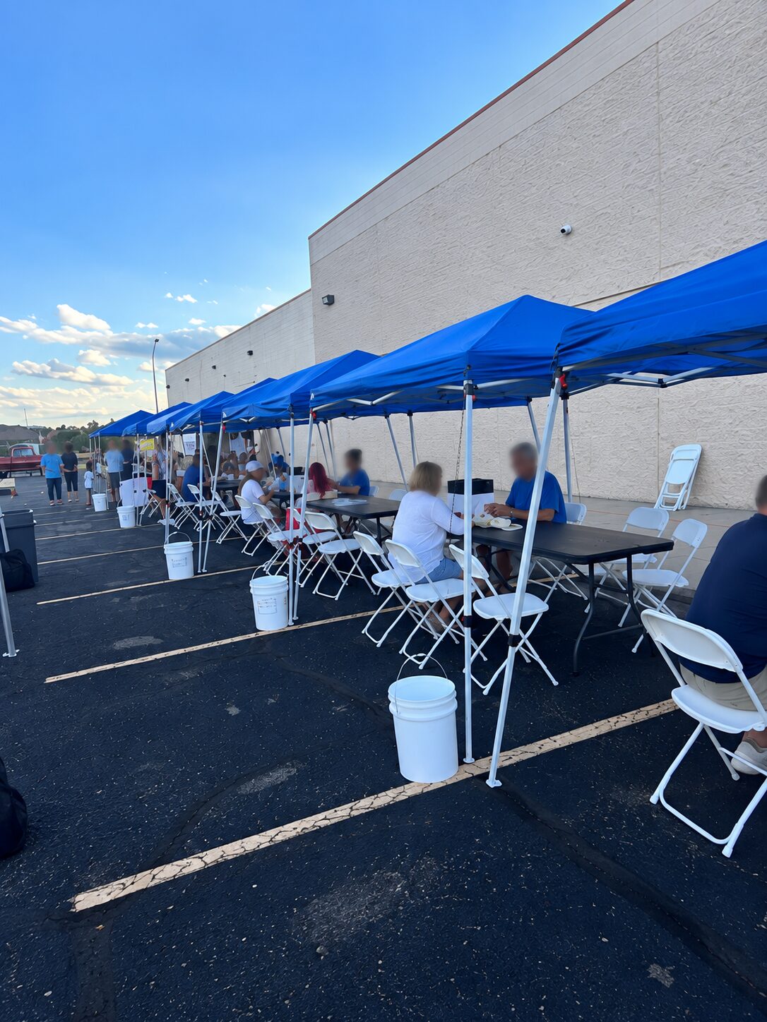Guests seated at tables under a row of blue event tents in Thornton
